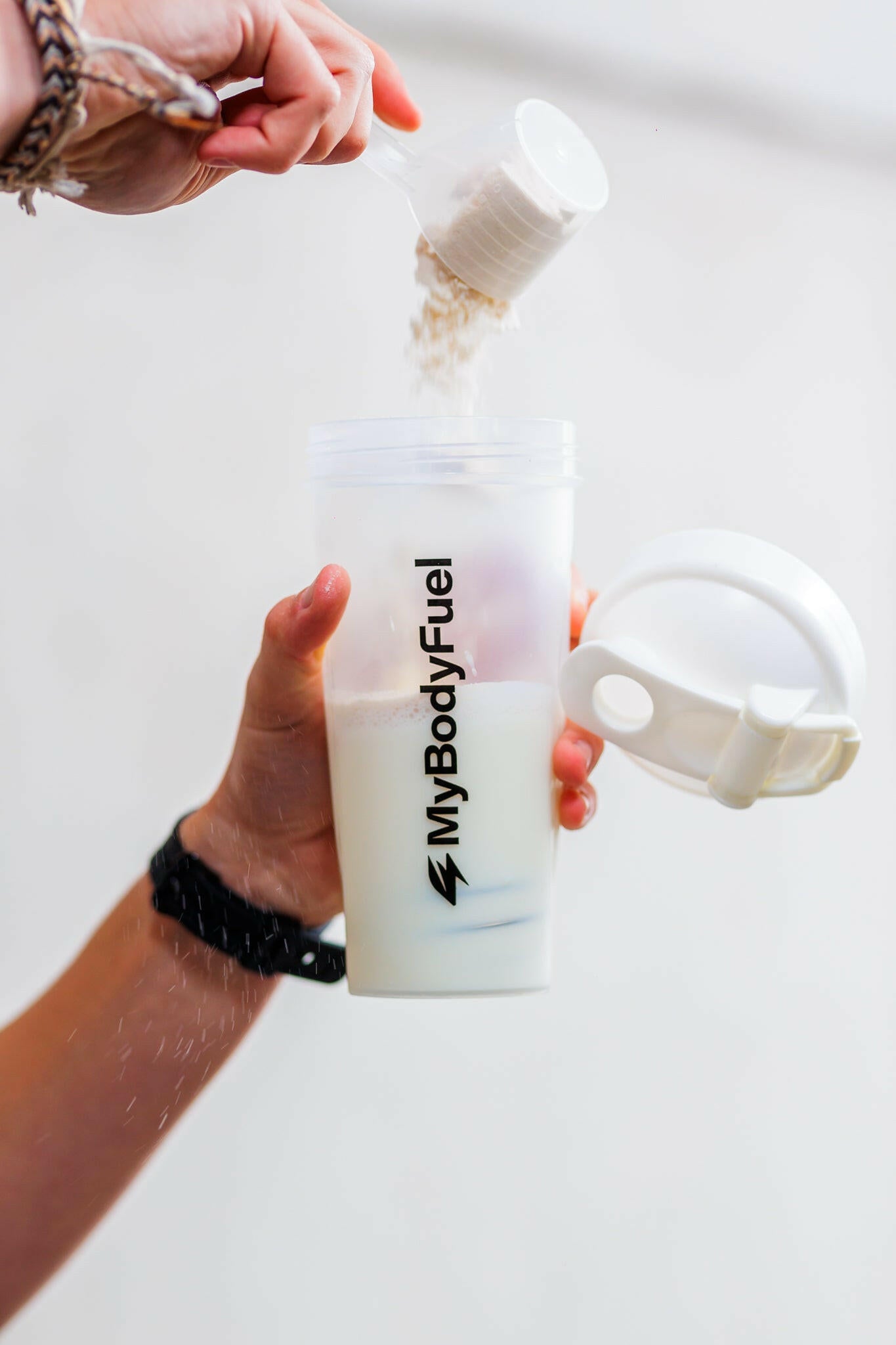 Persoon vult transparante MyBodyFuel shakebeker 700 ml met scoop proteïnepoeder en water