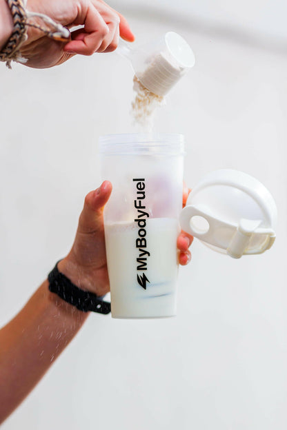 Persoon vult transparante MyBodyFuel shakebeker 700 ml met scoop proteïnepoeder en water